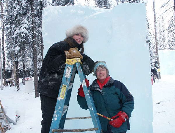 Allure, deep water fish by Heather Brown. Heather and Joan Brice standing in snow near a large ice block, just starting the sculpture.