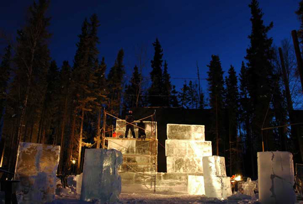 Animal Parade ice sculpture work site. “Site 5” at night. At the edge of the woods, ice blocks stacked, scaffolding, lights. By Steve Brice, Heather Brown, Tjana Raukar, and Mario Amegee. Ice Alaska 2005.