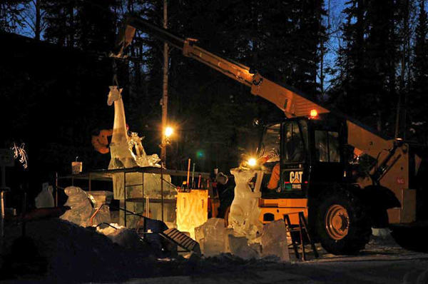 Animal Parade ice sculpture. “Site 5” at night. At the edge of the woods, ice blocks stacked, scaffolding, lights and hoists. By Steve Brice, Heather Brown, Tjana Raukar, and Mario Amegee. Ice Alaska 2005