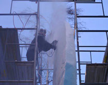 Ice carver on scaffolding using powertool, saw, to rough out the form. Ice Alaska, World Ice Art Championships, 2007.