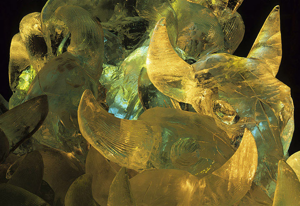 48 large buffalo skulls carved out of ice are stacked in a pile in this ice sculpture, called “Wascana,” by Patricia Leguen and team. Night view, lit with colored lights. For Ice Alaska event, photo by Patrick J. Endres at AlaskaPhotoGraphics.