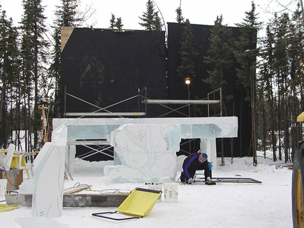 Work in progress “Birth of Blue Bird” ice sculpture by Junichi Nakamura and team. See the template adhered to the ice block, artist working, daytime.