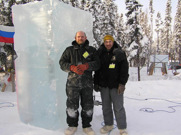 Artists, Validmir Zhikhartsev and Vitality Lednv standing next to a large ice block, block standing verically. Ice Alaska World Ice Art Championships