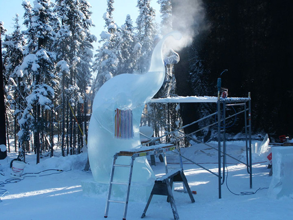 Fiddler in progress, artists on scaffolding, daylight, black cloth hung in trees to block the sun. World Ice Art Championships, ladimir Zhikhartsev and Vitaliy Lednev artists.