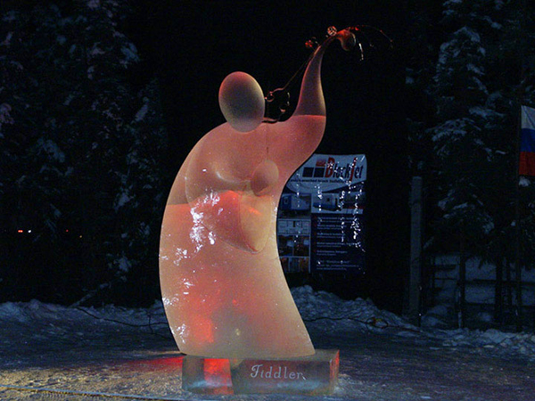 Fiddler finished, at night under orange lights. Dark woods in background. Artists: Vladimir Zhikhartsev and Vitaliy Lednev 2006, World Ice Art Championships.